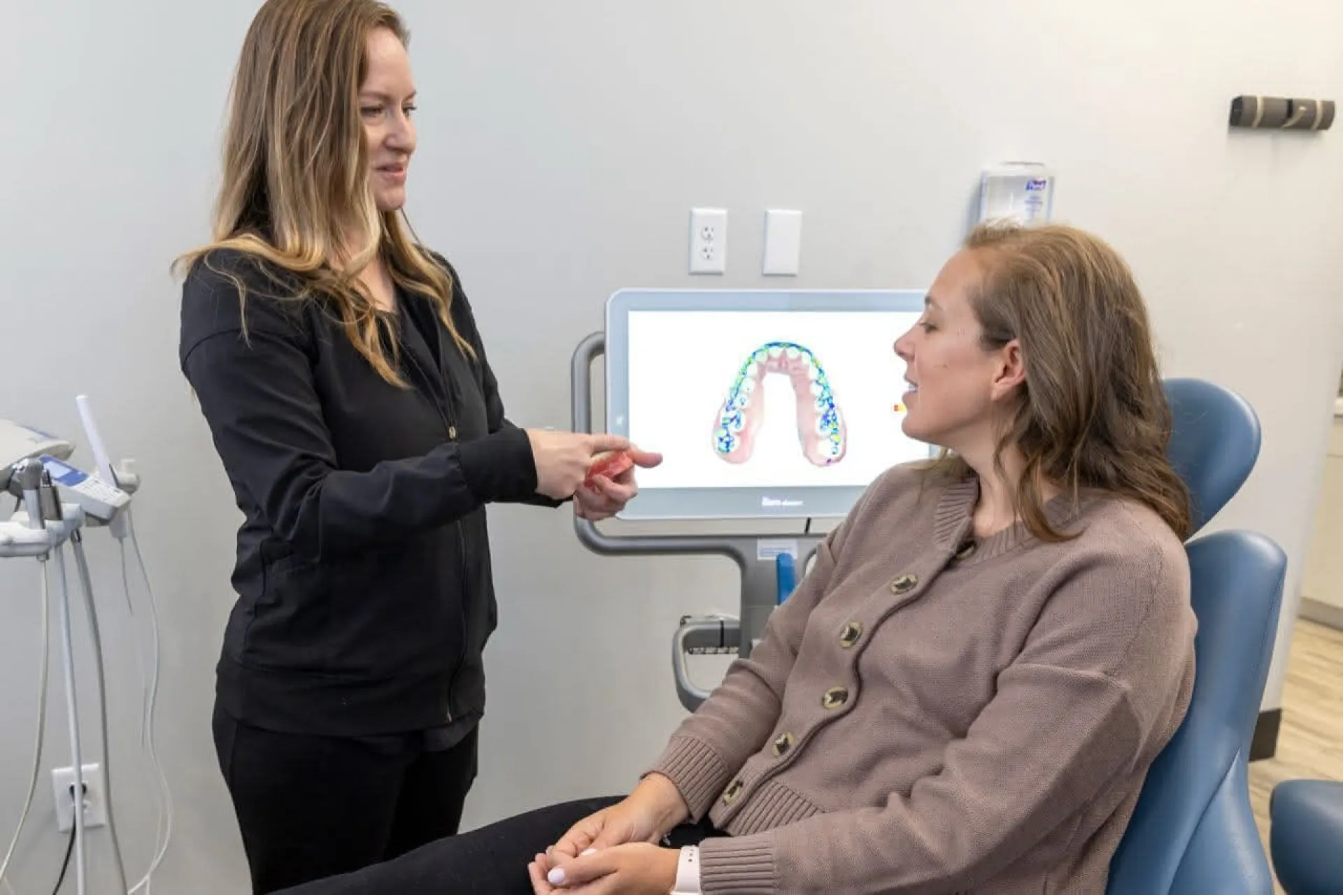 A dental assistant show a patient an example in front of an X-ray