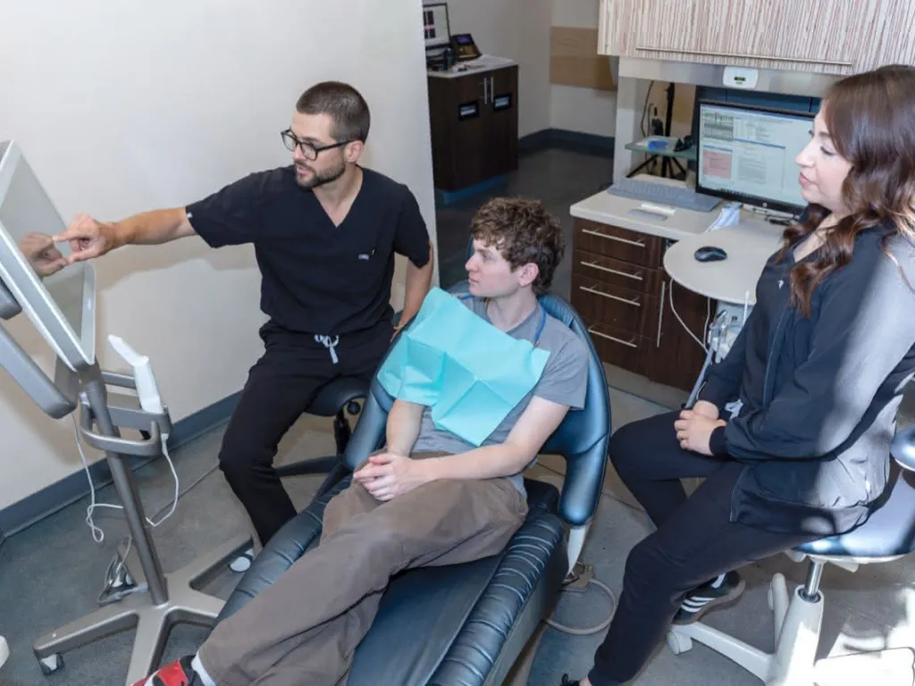 A doctor pointing at a monitor with a patient in a chair