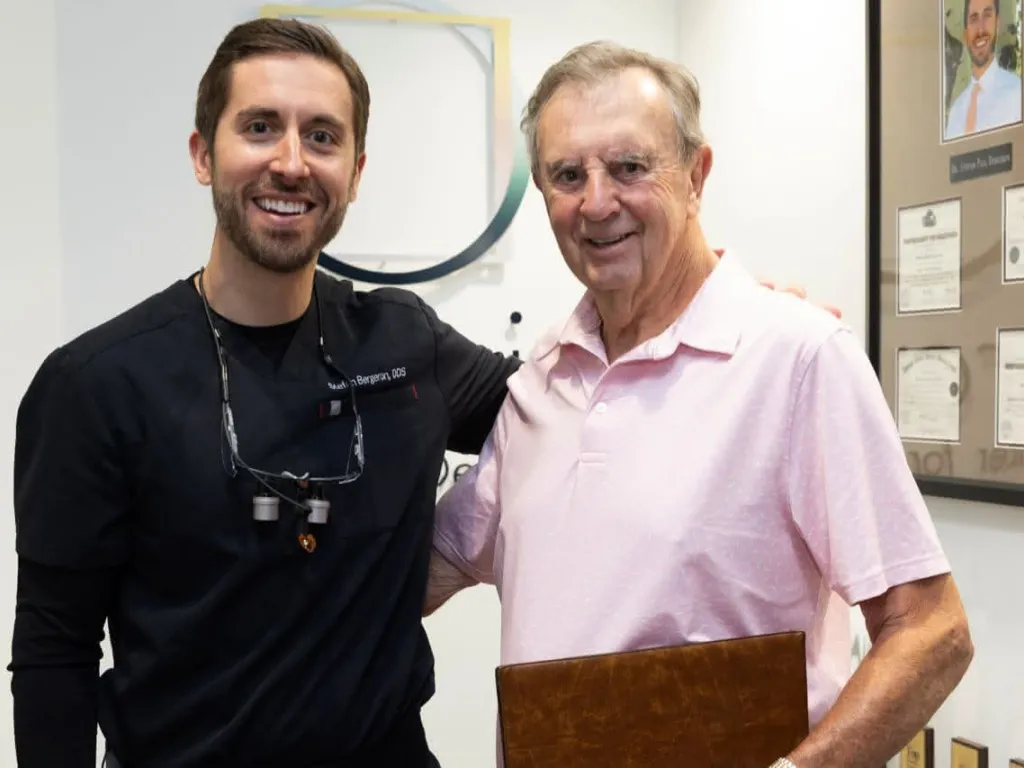 A dentist with a patient in a pink shirt holding a folder