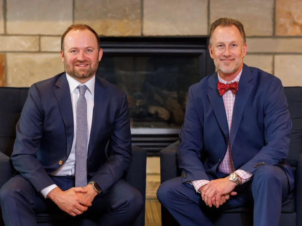 Two doctors in suits in front of a fireplace