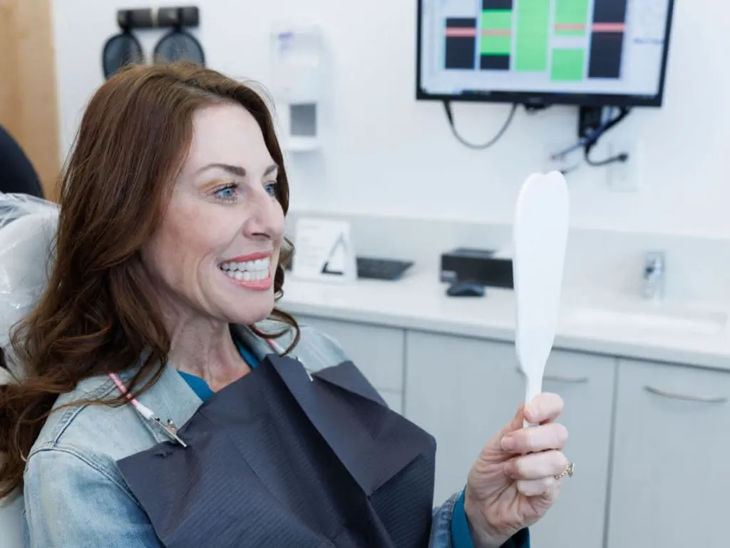 A patient holding a hand mirror smiling