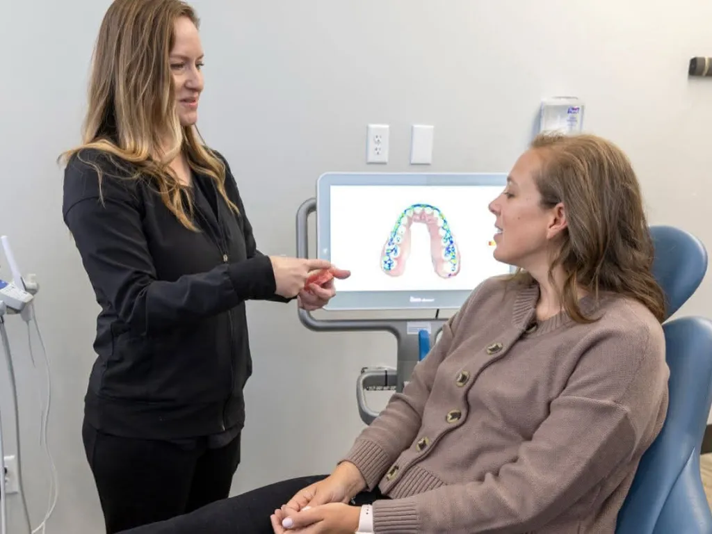 A dental assistant show a patient an example in front of an X-ray