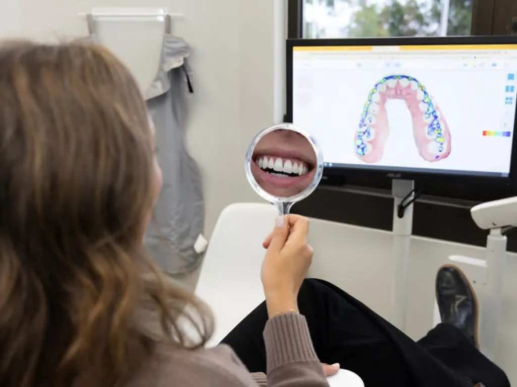A patient holdind a hand mirror in front of a computer