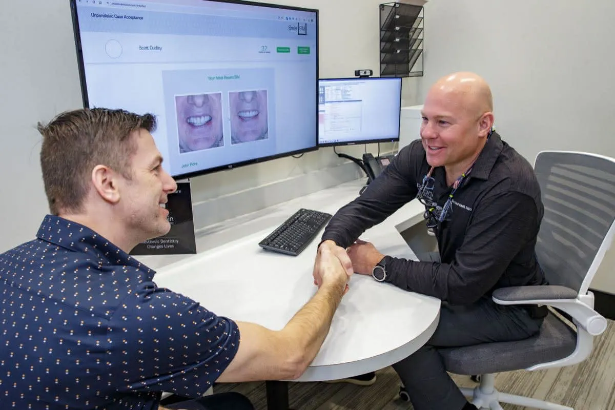 Dentist shakes hand with a patient at a desk