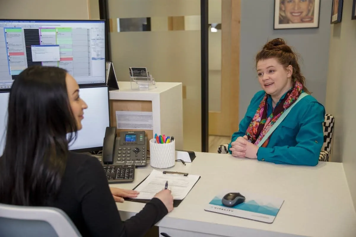 A patient discusses things with a staff member at the front desk
